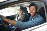 Ein junger Mann und eine junge Frau sitzen in einem Auto und lachen.